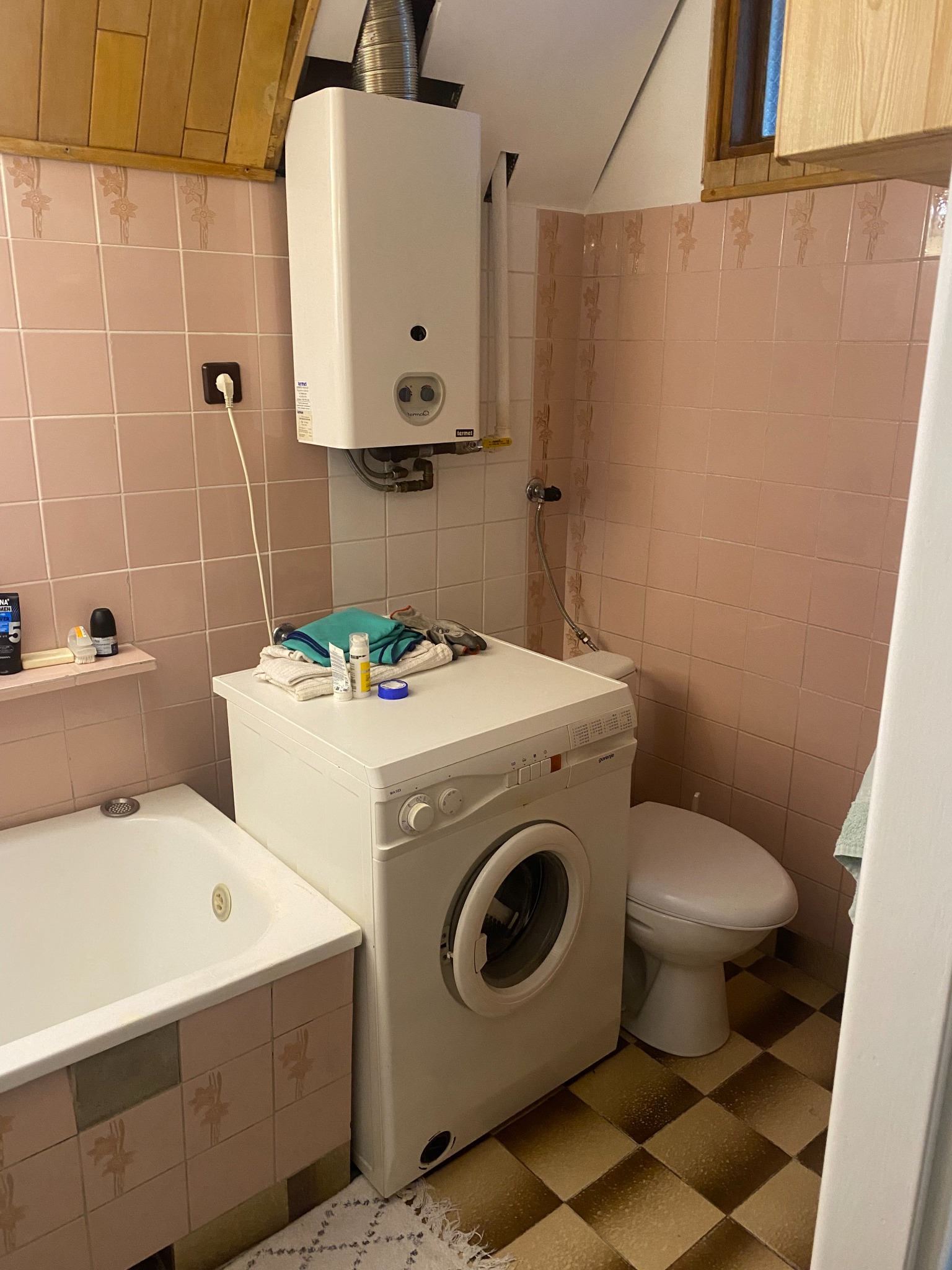 Łazienka przed remontem — widok na pralkę, WC i piecyk